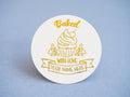 Add a touch of sweetness with our bakery sticker! Featuring a charming cupcake, 'Baked with Love' wrapped around it and a customizable banner for your bakery name—all embossed in elegant gold. Perfect for boosting your business's visibility!