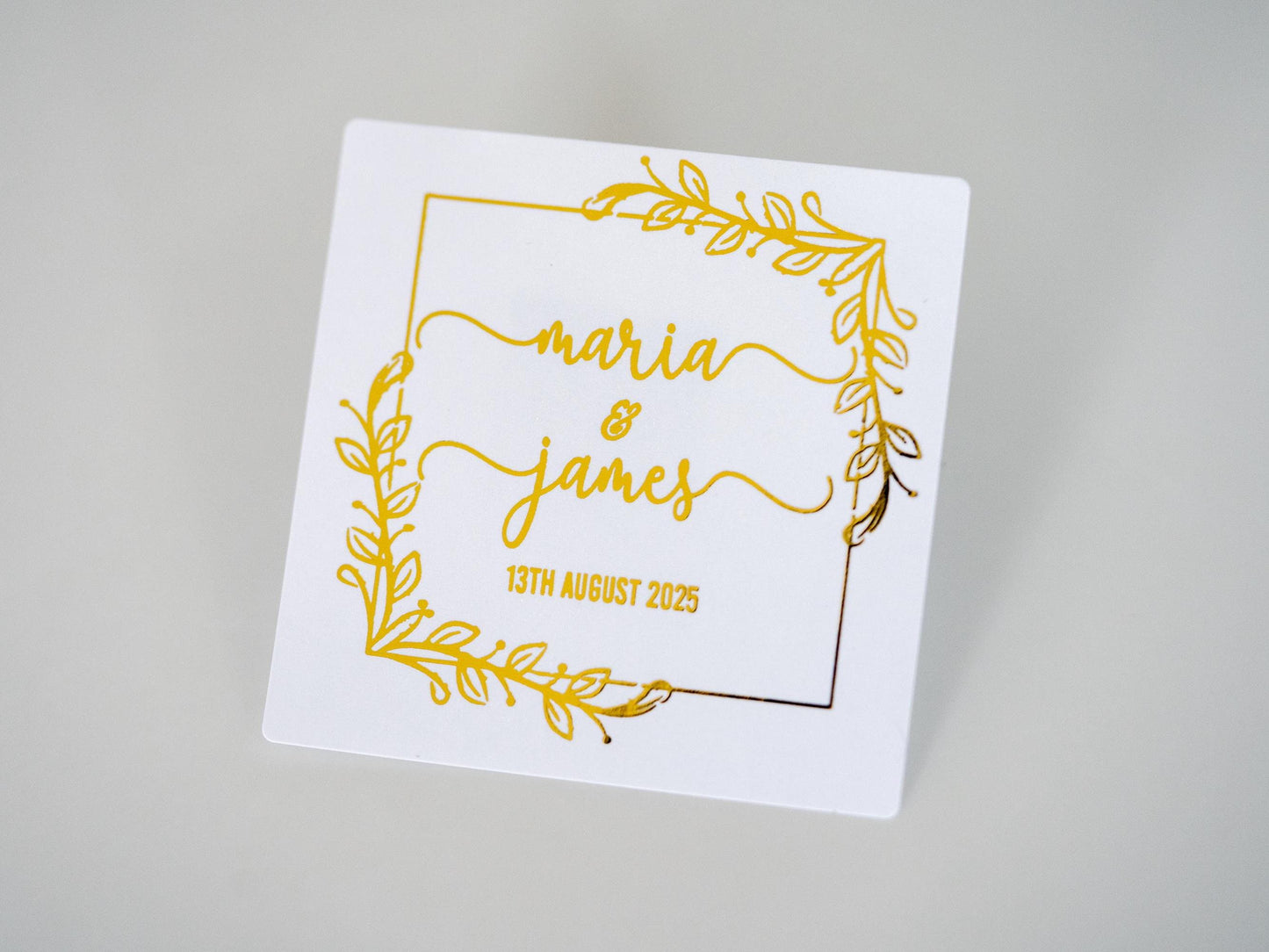 A square sticker with a leaf border around the edges. The names of the happy couple in a lovely handwritten font and the wedding date at the bottom of the names. The design is adorned with a lovely metallic foil for an amazing shine.