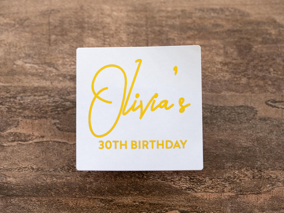 A square sticker with the birthday person's name in a lovely handwritten font. The age is written under the name in a straight font and the entire design layered in a lovely gold foil. The foil shines perfectly in light.