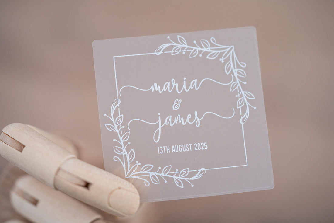 Frosted clear square sticker with a leaf square border. The names of the happy couple sit in the middle of the sticker using a lovely handwritten font. The wedding date finishes the sticker, the sticker is printed using a lovely white ink.