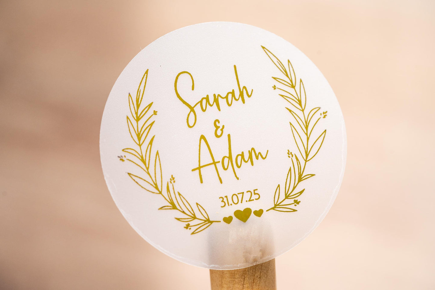 Personalised wedding sticker with the happy couples name in the middle of the sticker using a lovely handwritten font. The date sits under the names and a leaf frame surrounds the name with hearts at the bottom. Gold foil is added for a lovely shine
