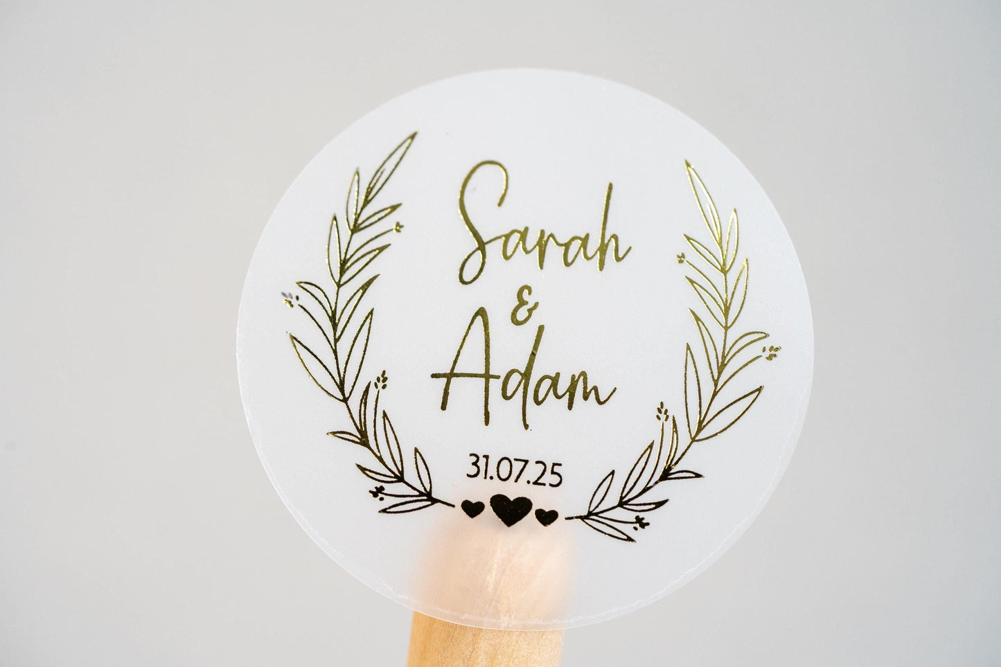 Personalised wedding sticker with the happy couples name in the middle of the sticker using a lovely handwritten font. The date sits under the names and a leaf frame surrounds the name with hearts at the bottom. Gold foil is added for a lovely shine