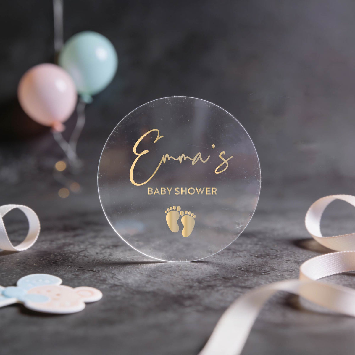 Clear transparent round sticker with 'Emma's Baby Shower' text in gold foil.