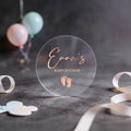 Clear transparent round sticker with 'Emma's Baby Shower' text in rose gold foil.