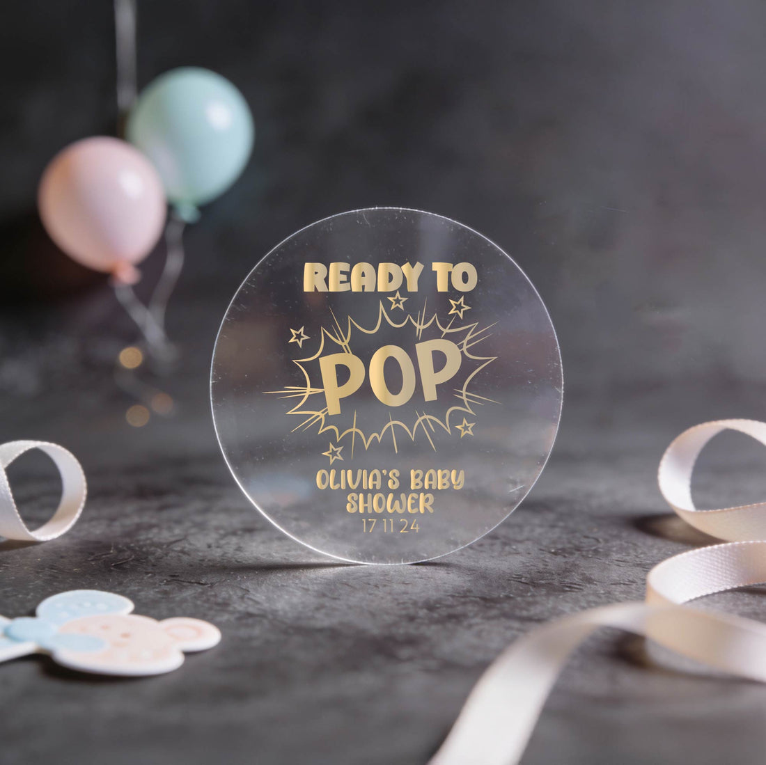 A transparent round sign reads "Ready to Pop" in gold foil letters, surrounded by stars. It announces "Olivia's Baby Shower" with the date "17 11 24."