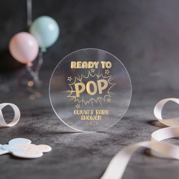 A transparent round sign reads "Ready to Pop" in gold foil letters, surrounded by stars. It announces "Olivia's Baby Shower" with the date "17 11 24."