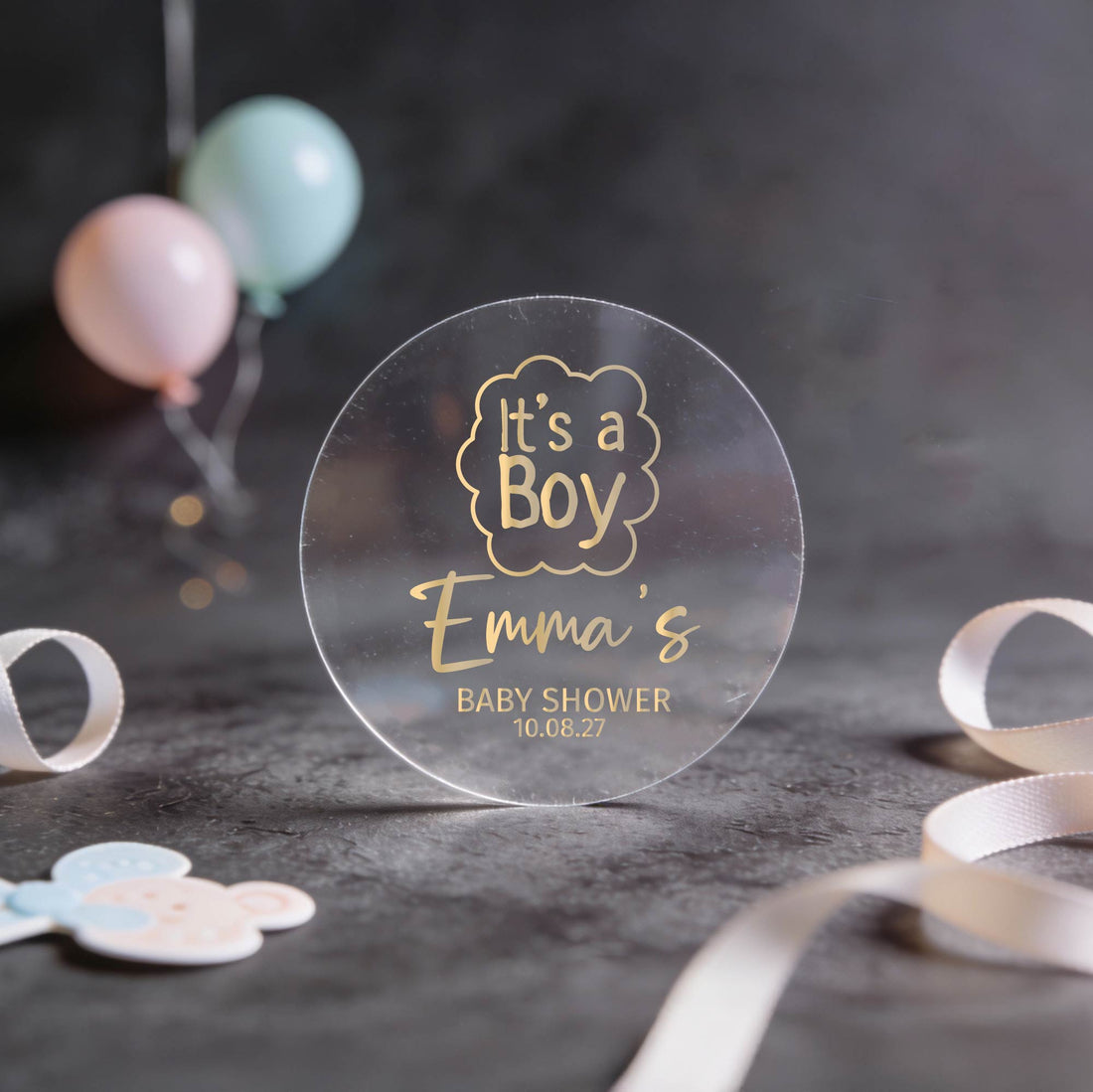 A transparent sticker with 'It's a Boy Emma's Baby Shower' text written in gold foil.