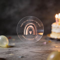 A clear round party favour sticker with a rose gold foil rainbow and heart design reads 