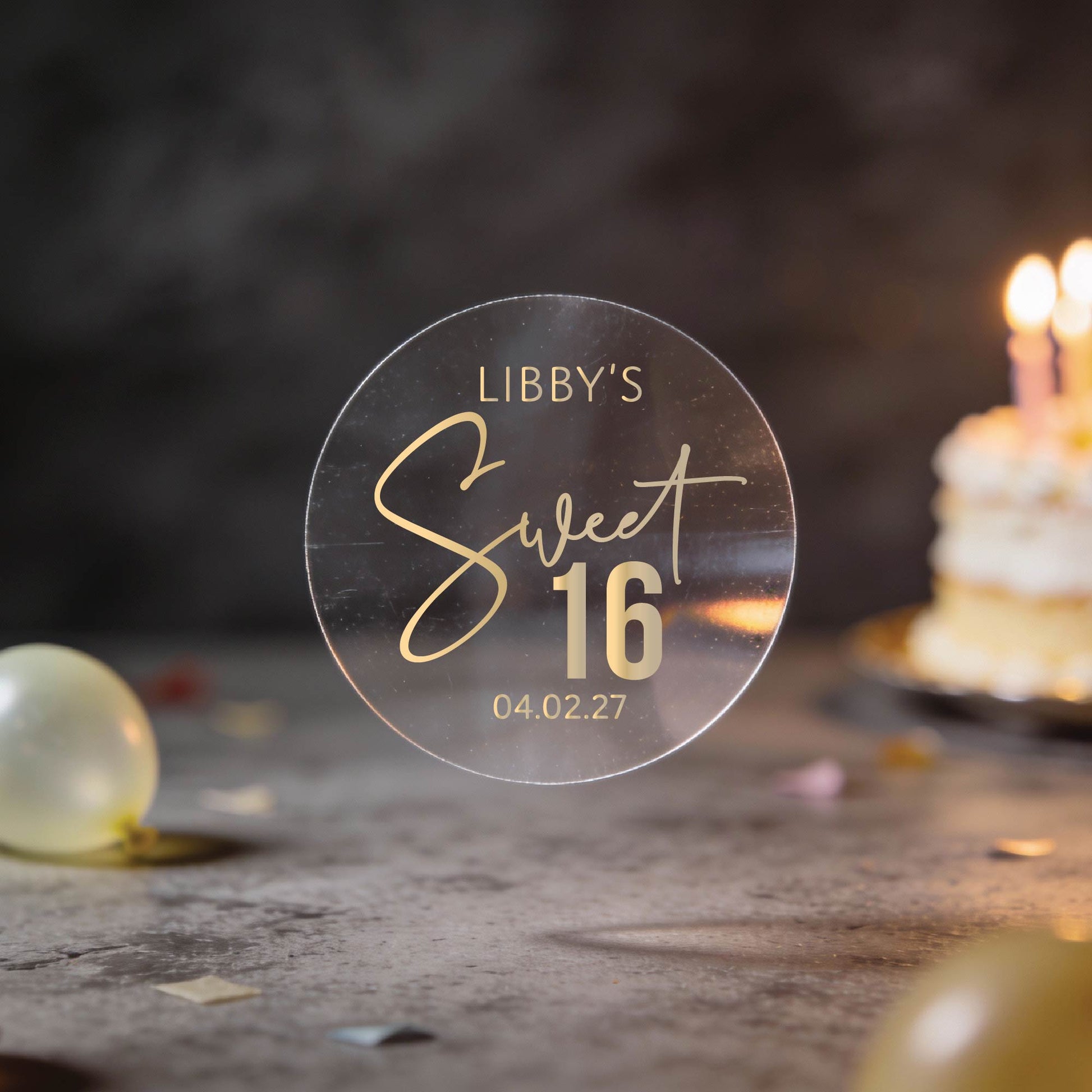 A Transparent round sticker with "Libby's Sweet 16" written in elegant script with gold foil and the date at the bottom. 