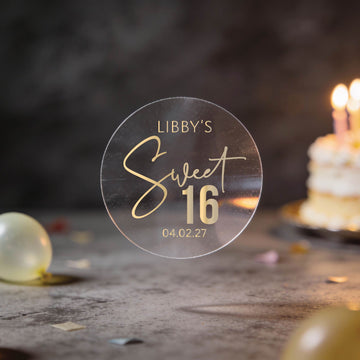 A Transparent round sticker with "Libby's Sweet 16" written in elegant script with gold foil and the date at the bottom. 
