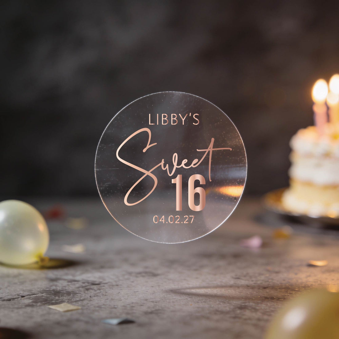 A Transparent round sticker with "Libby's Sweet 16" written in elegant script with gold foil and the date at the bottom. 