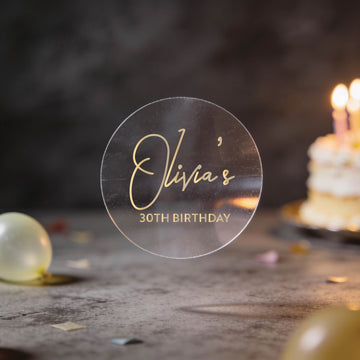 A transparent clear stickers with "Olivia's 30th Birthday" written in gold foil.