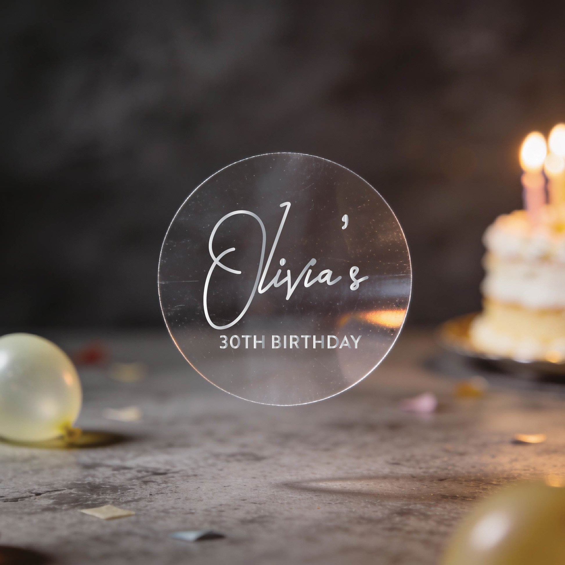 A transparent clear stickers with "Olivia's 30th Birthday" written in silver foil.