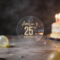 A round transparent sticker with gold foil text reading 'Amelia's 25th Birthday' and gold stars surrounding the design