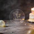 A clear round with gold foil text reading 'Fifty & Fabulous' & 'Amelia's 50th Birthday'. 