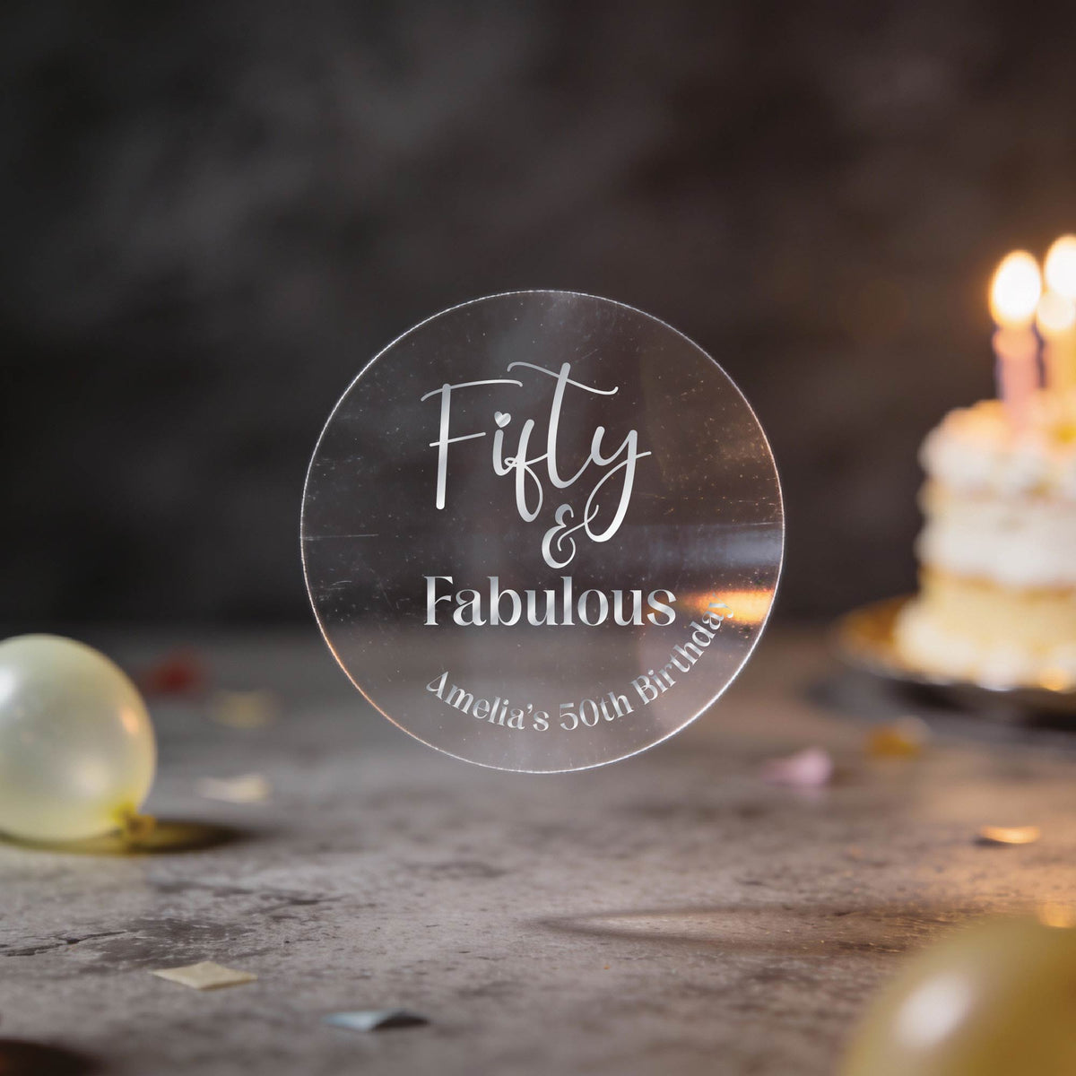 A clear round with silver foil text reading 'Fifty & Fabulous' & 'Amelia's 50th Birthday'. 