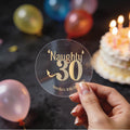 A hand holds a clear round sticker with gold foil lettering that reads 