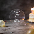 A clear round silver foil sticker and the text 'Emma's 1st Birthday'. There is a large number 1 with eyes and a smile in the middle of the sticker.