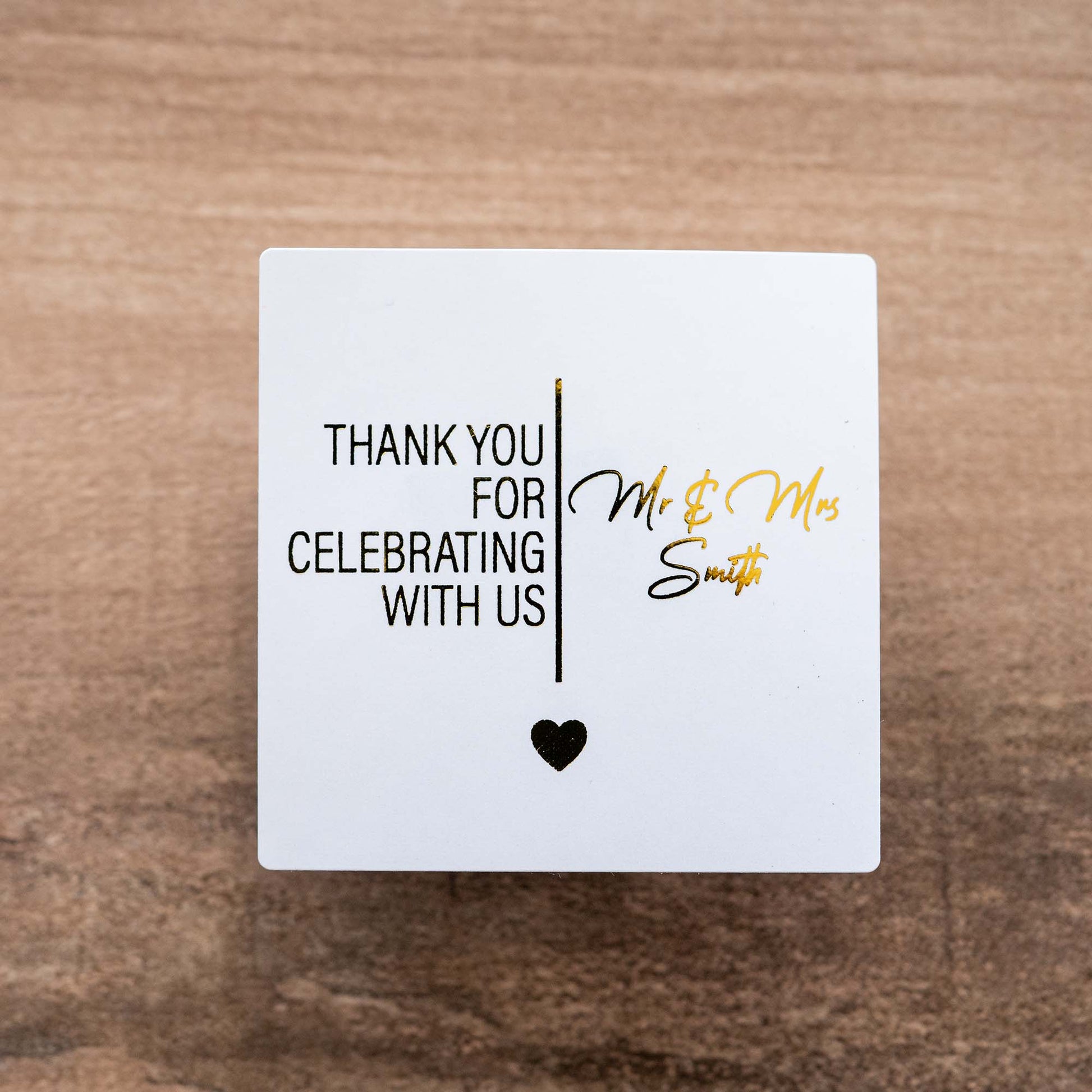 White square sticker with "Thank you for celebrating with us and the name of the married couple in gold foil. 