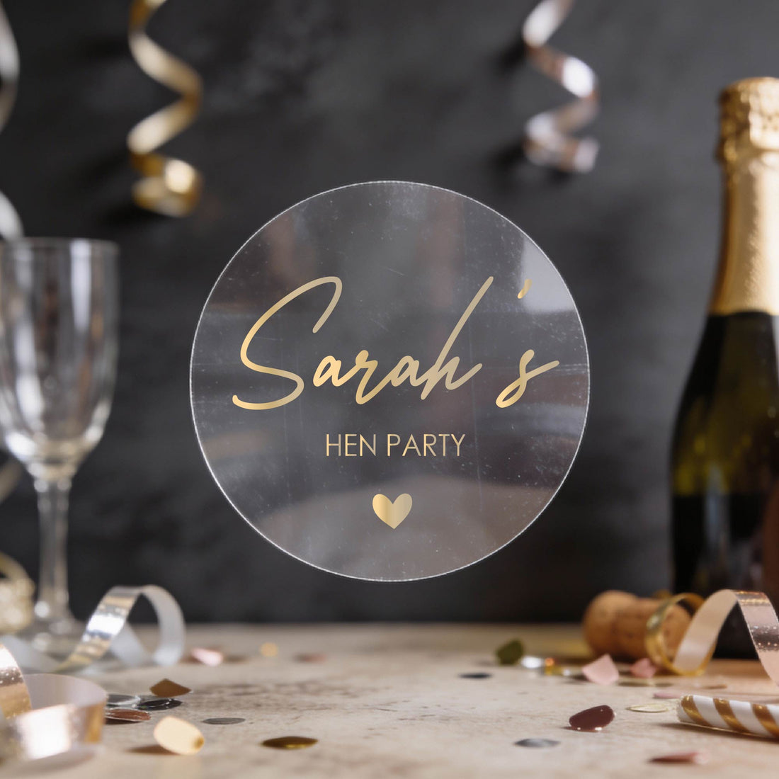 Personalised 'Sarah's Hen Party' round transparent sticker written in gold foil. 