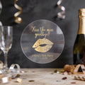 A round clear sticker with gold foil text reading 'Kiss the miss goodbye!' and a gold lips graphic, displayed on a party table with a champagne bottle, glass, and confetti in the background.