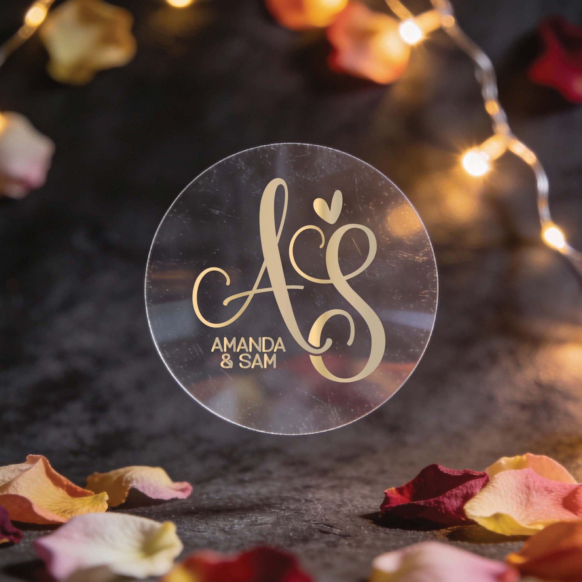 A round, transparent sticker with elegant gold foil initials "A & S" and a heart, set against a dark background. Surrounded by fairy lights and rose petals, conveying a romantic atmosphere.