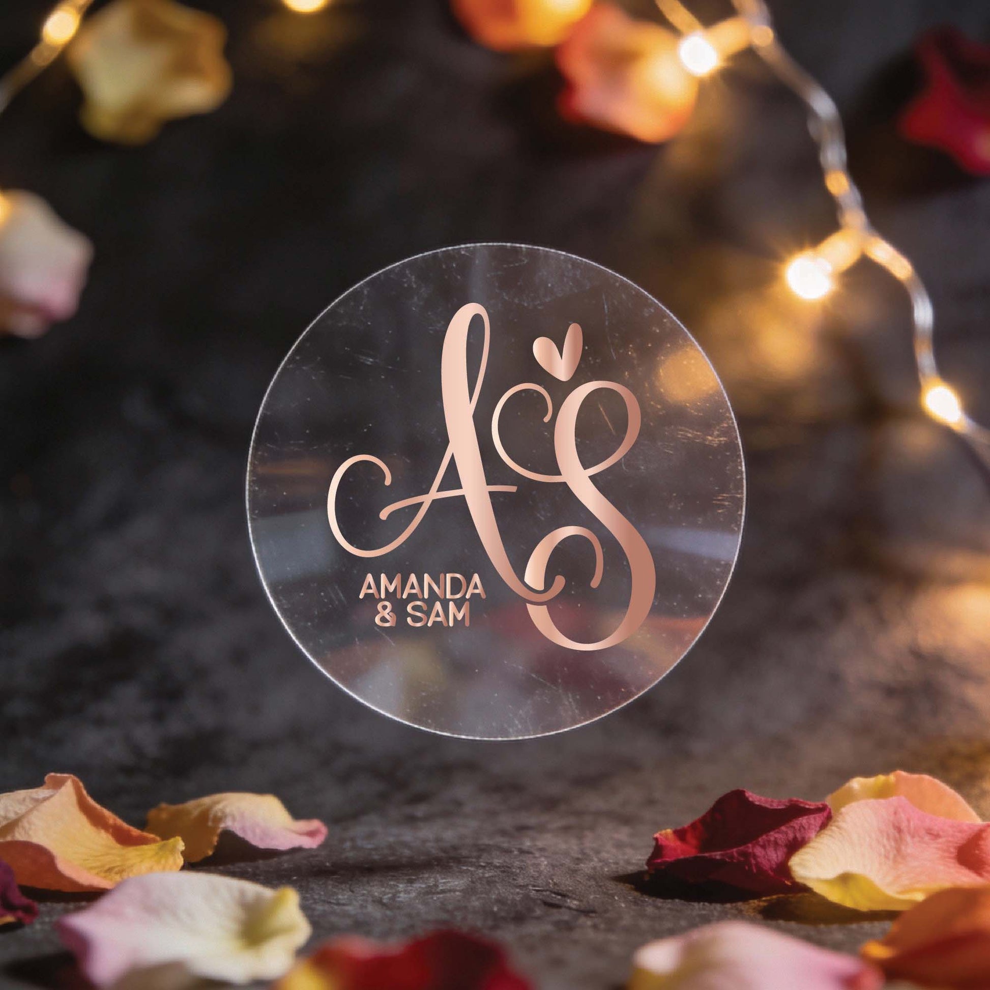 A round, transparent sticker with elegant rose gold foil initials "A & S" and a heart, set against a dark background. Surrounded by fairy lights and rose petals, conveying a romantic atmosphere.