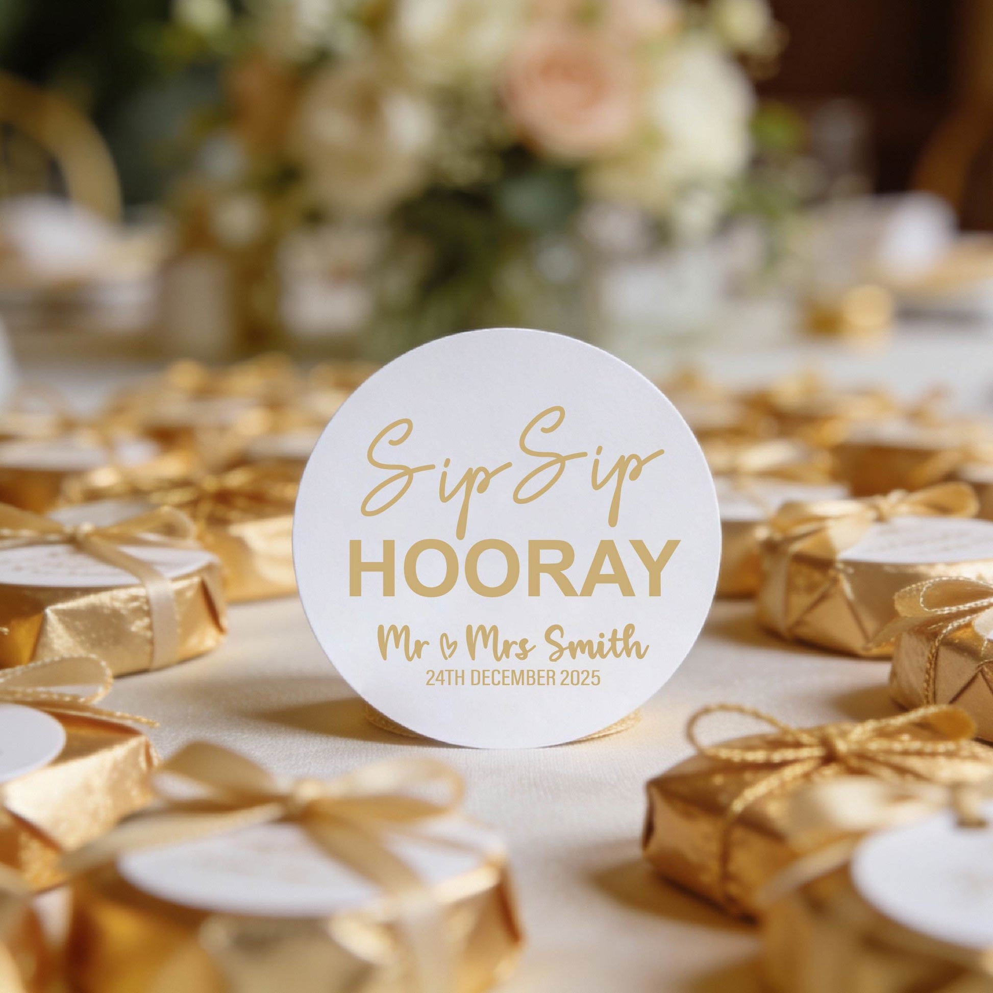 A round white stickers which has  "Sip Sip Hooray" in the centre and the name of the happy couple and date underneath written in gold foil. 