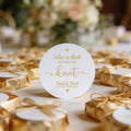 A white gloss round sticker with gold foil text reading, 