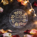 A round, clear sticker with gold foil leaf design and the words 