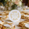 A round, white gloss sticker with gold foil leaf design and the words 