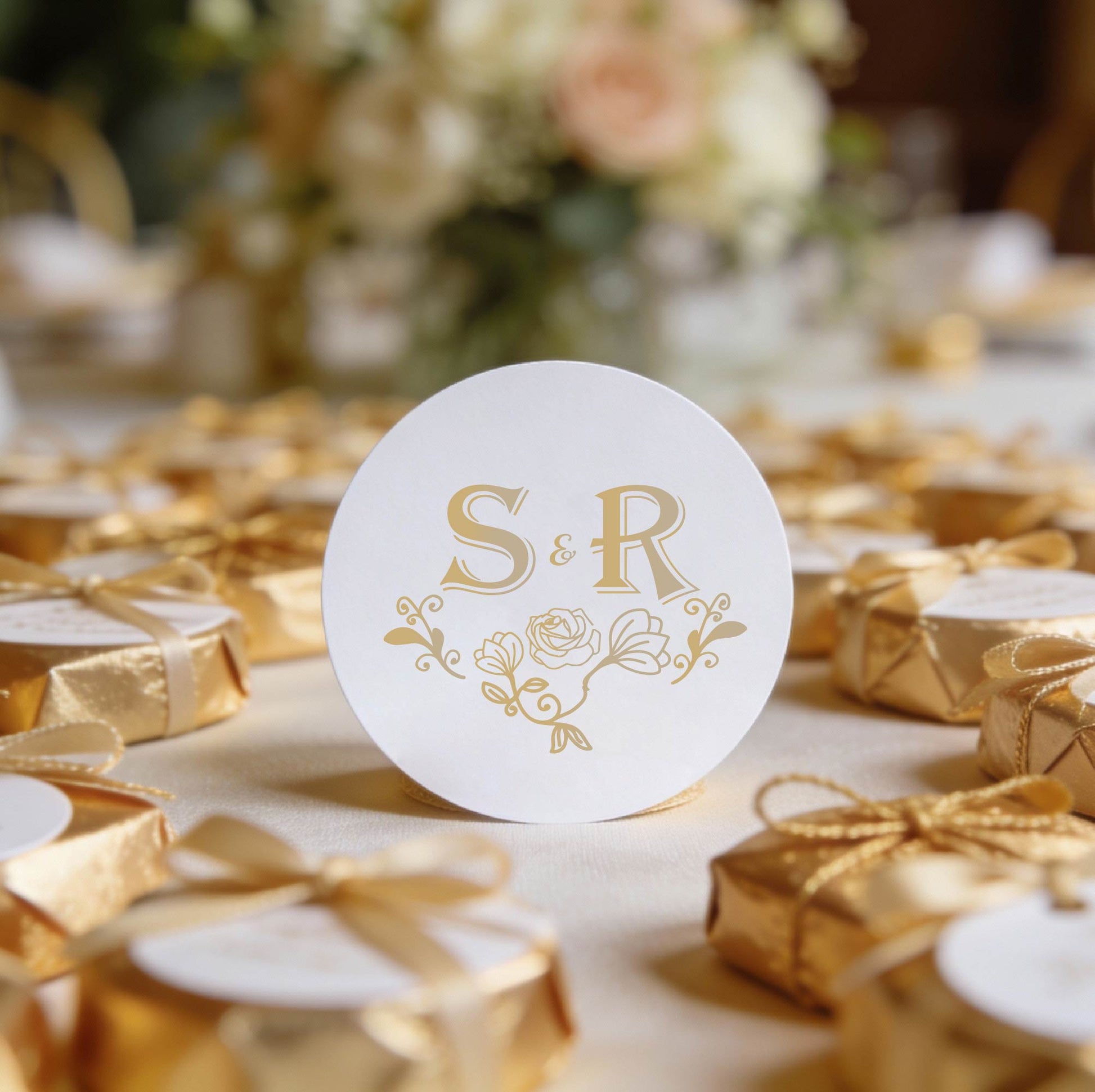 A round, white gloss sticker with gold foil initials "S & R" and floral design in the centre.
