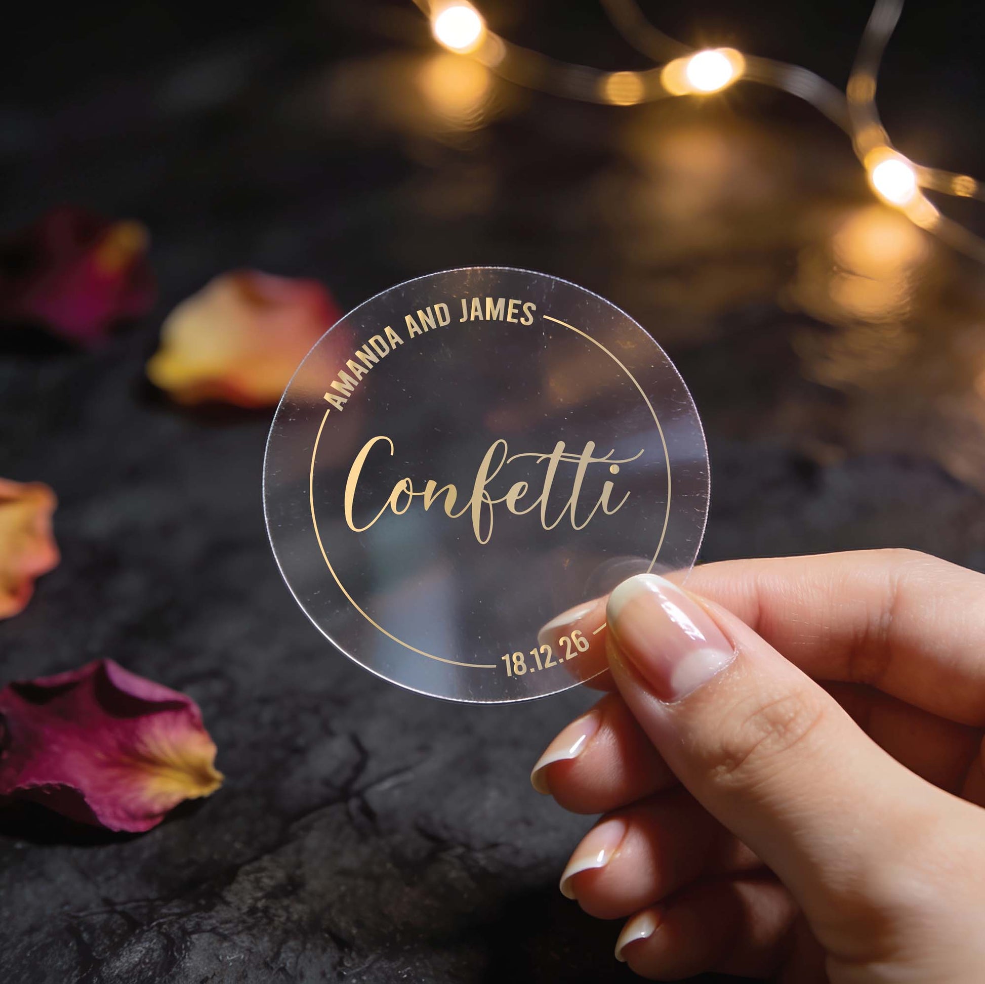 A Transparent round wedding sticker with "Confetti" in elegant gold foil script written in the middle, a round circle goes around the word with the names of the happy couple on the top and the wedding date at the bottom. 