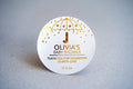A round white sticker with gold foil details, personalised with the name 'Olivia' for a baby shower event. The sticker includes a thank you message and a date.