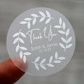 A custom round white sticker with a 'Thank You' message, leaf design, and personalised text including names and a date.