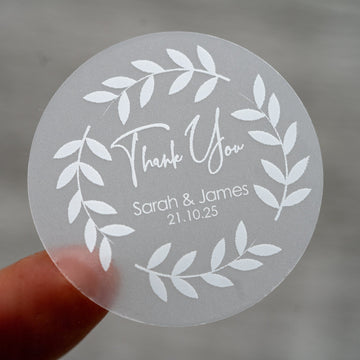 A custom round white sticker with a 'Thank You' message, leaf design, and personalised text including names and a date.