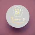 A round sticker with 'It's a Girl' and the name 'Emma's' printed on it with gold foil, indicating it's for a baby shower.