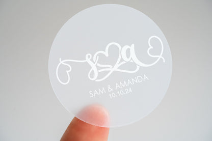 This elegant frosted clear monogram sticker features personalised initials in a stylish handwriting font, crafted in white. An infinity symbol at the centre signifies eternal love, flanked by charming hearts. Ideal for custom gifts or wedding favours
