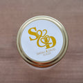 A close-up of a round, white sticker with a gold monogram design and the text 'S & D' in an elegant script, along with the names 'SARAH & DAVID' and a date '10.10.24'.