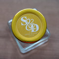 A close-up of a round clear sticker with a custom white monogram print of a couple's initials and names.