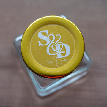 A close-up of a round clear sticker with a custom white monogram print of a couple's initials and names.