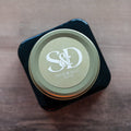 A round, white monogram sticker with a gold border applied to a clear glass jar lid.