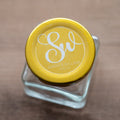 A clear round sticker with a monogrammed design on a glass jar, presenting a personalized and elegant appearance.