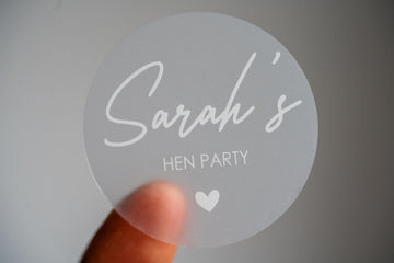 This frosted clear hen party sticker features the bride-to-be's name in elegant white ink using a handwriting font. Perfect for hen party favours, bridal shower décor or gift bags. This personalised sticker adds a unique touch to your celebration.