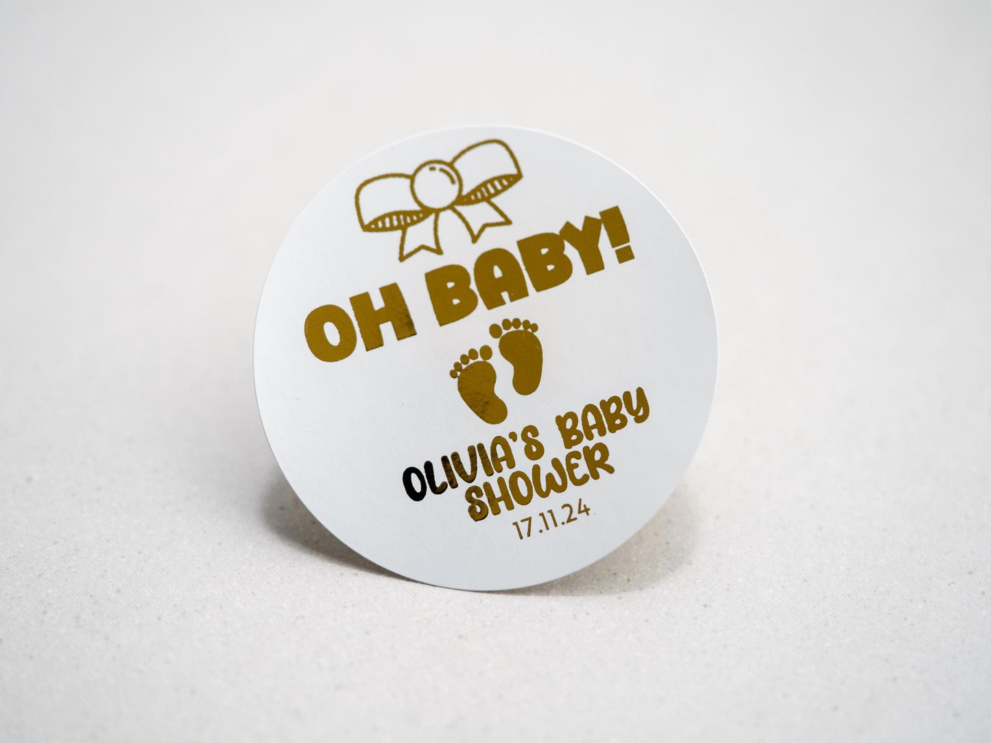 Our elegant baby shower sticker features a gold embossed design with a charming bow on top, &quot;Oh Baby&quot; in the centre, and adorable baby footprints underneath. Personalize with the mother-to-be&#39;s name and date for a perfect touch