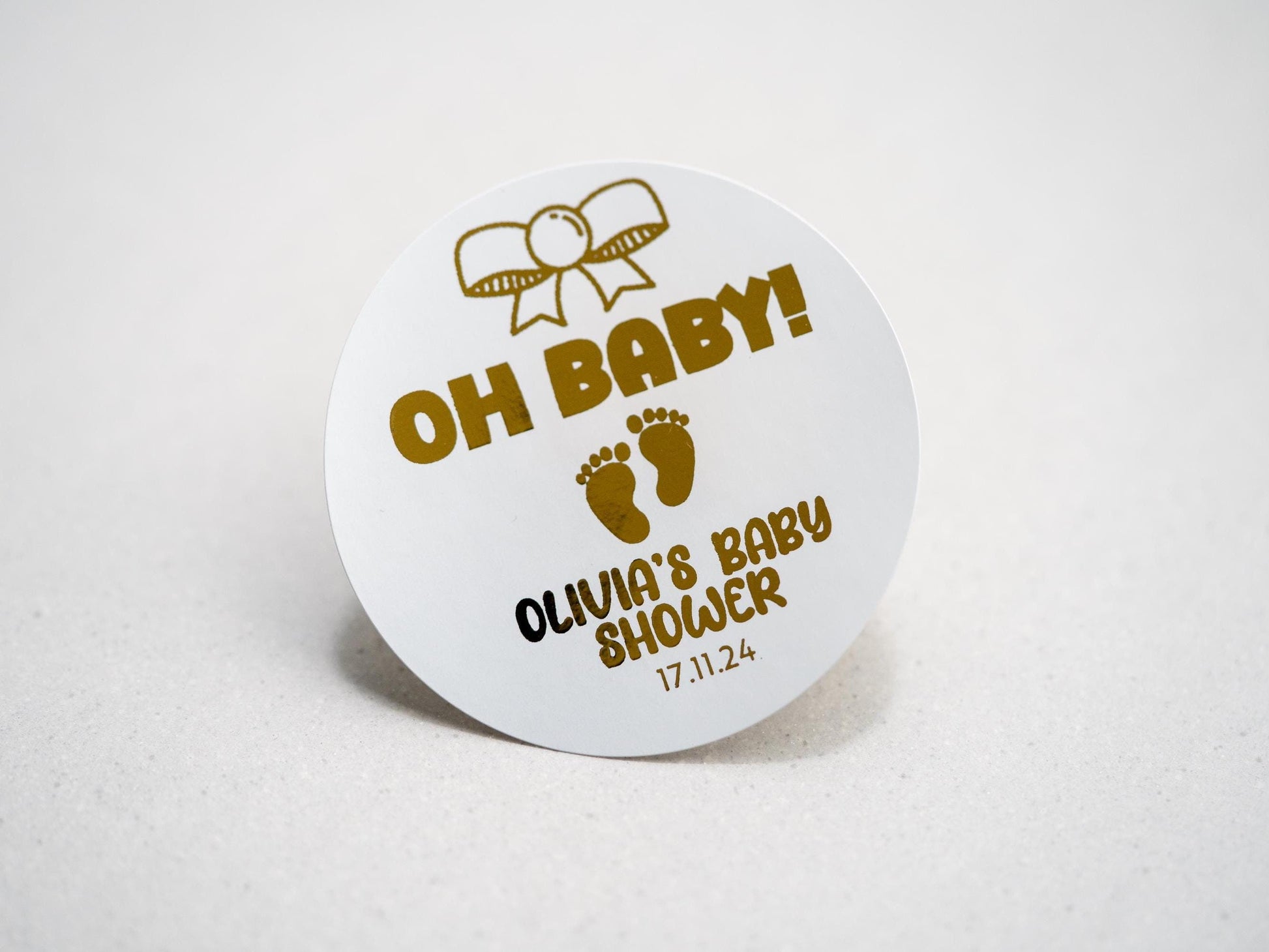 Our elegant baby shower sticker features a gold embossed design with a charming bow on top, &quot;Oh Baby&quot; in the centre, and adorable baby footprints underneath. Personalize with the mother-to-be&#39;s name and date for a perfect touch