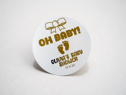 Our elegant baby shower sticker features a gold embossed design with a charming bow on top, &quot;Oh Baby&quot; in the centre, and adorable baby footprints underneath. Personalize with the mother-to-be&#39;s name and date for a perfect touch