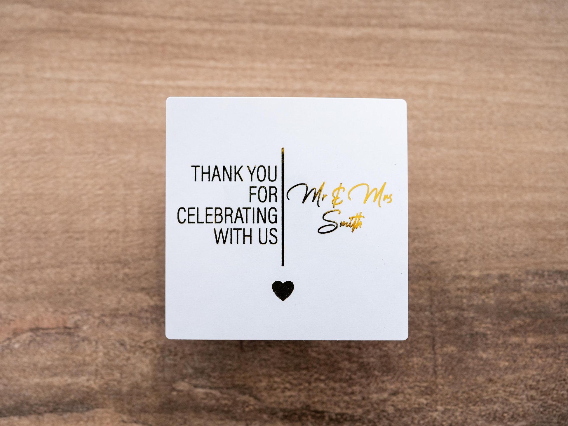 Personalised square metallic foil stickers with &quot;Thank you for celebrating with us&quot; and the name of the lovely couple in the middle. The words are separated by a line and a heart finishing off the design at the bottom.