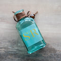 Blue bottle with 'S/R' monogram with gold foil print on a frosted clear square sticker.