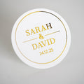 A round white sticker with gold metallic foil text personalised with the names 'Sarah & David' and a date '24.12.25'.